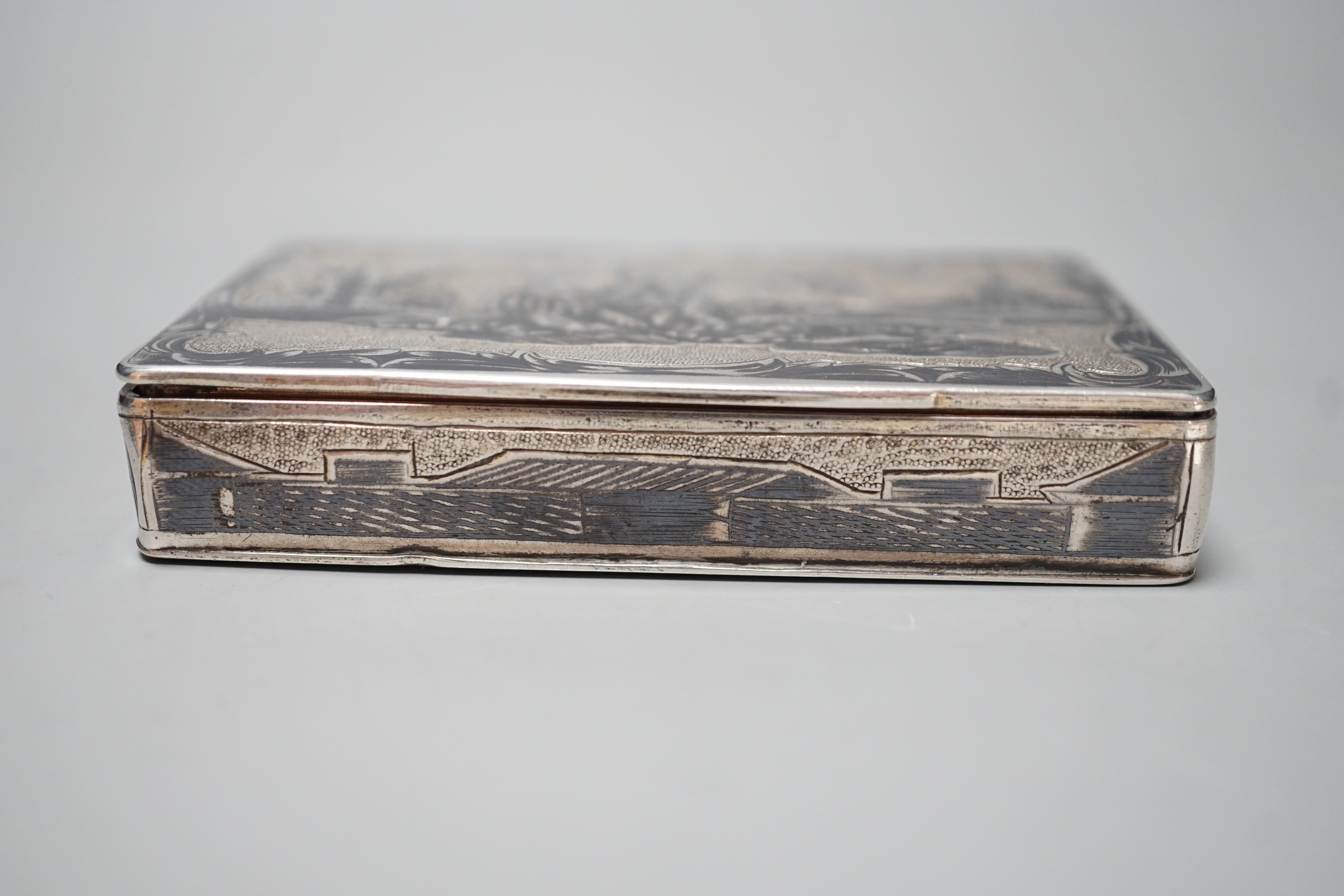 A late 19th century Russian 84 zolotnik and niello snuff box, decorate with figures in a landscape, 85mm.